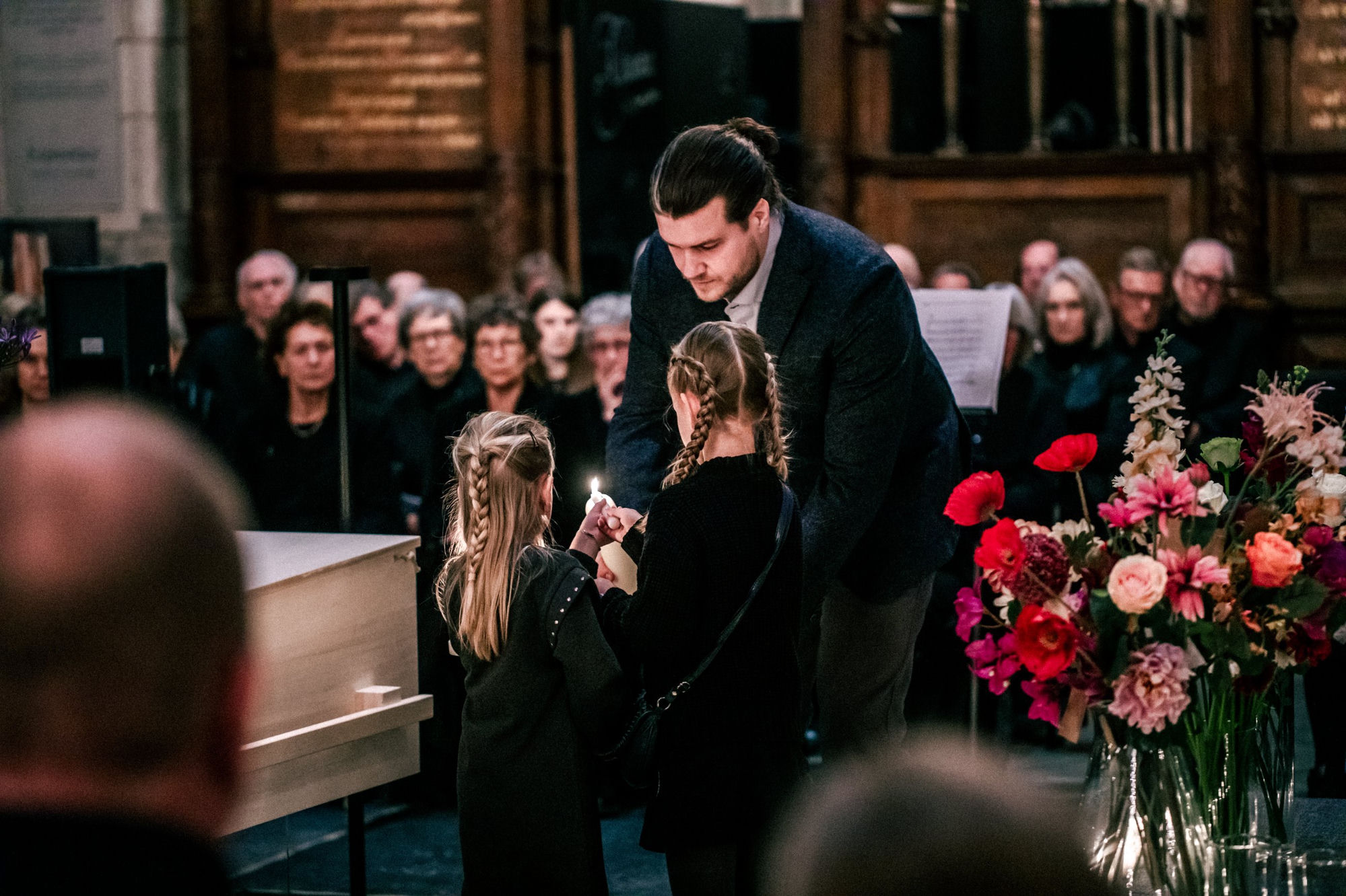 Bram Oudenampsen steekt samen met twee kinderen een kaars aan tijdens een uitvaartdienst